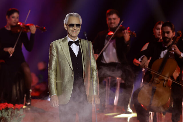 Andrea Bocelli standing on a stage, a band surrounding him.