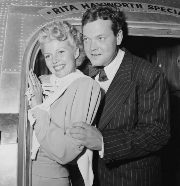 Rita Hayworth and Orson Welles pose for a photo together from the door of a plane.