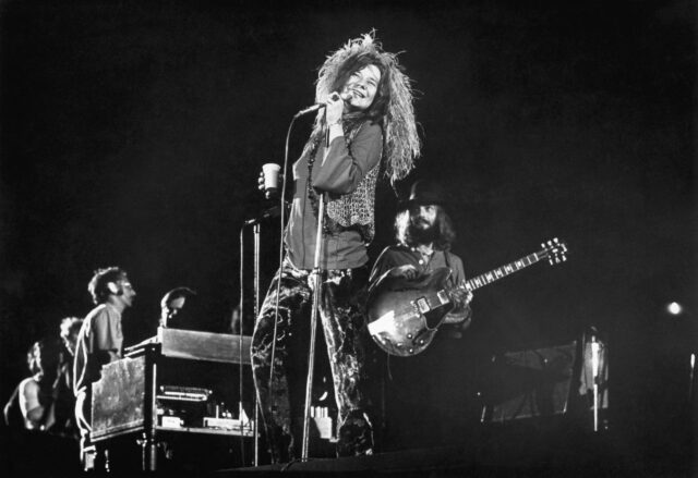 Janis Joplin performing on stage with a band behind her.