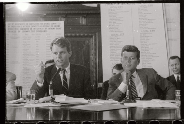 Robert Kennedy and John F. Kennedy sitting beside one another in a Senate hearing.