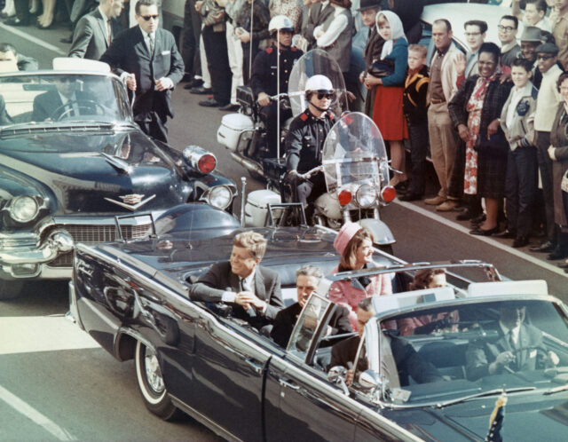 John F. Kennedy and Jackie Kennedy in a black convertible car.