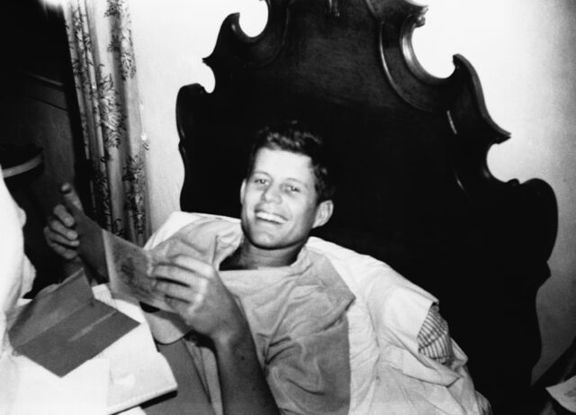 JFK laying in bed reading some mail.