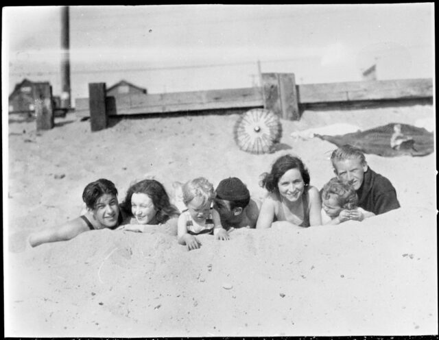 Gladys Pearl Baker and Norma Jeane Mortensen lying on the beach with a group of friends