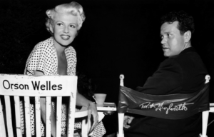 Rita Hayworth and Orson Welles sitting in chairs with each others' names written on the back.