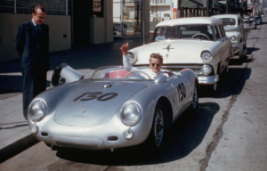 James Dean giving a thumbs up from his silver Porsche.