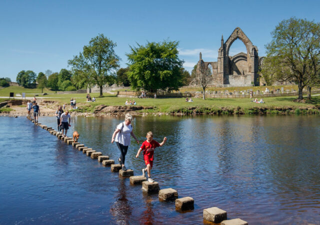 People walking across rocks spanning the River Wharfe