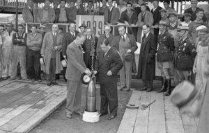 People watch as two men lower a time capsule into the ground.