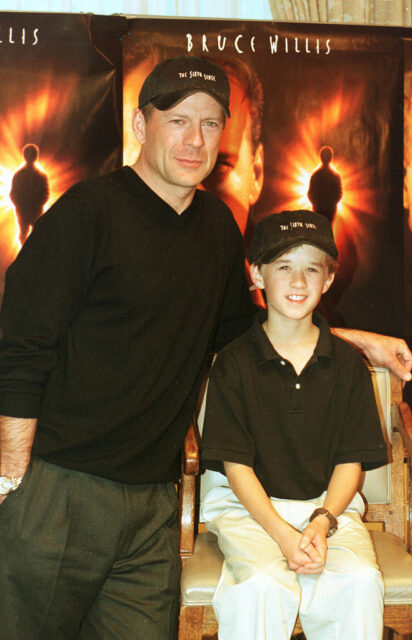 Bruce Willis and Haley Joel Osment standing in front of posters for 'The Sixth Sense'