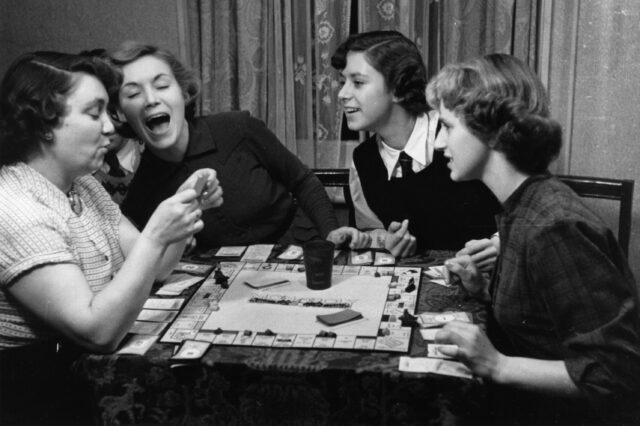 A group of women sitting at a table playing Monopoly.