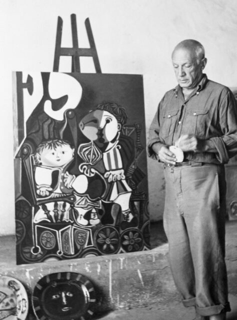 Pablo Picasso standing beside an easel with one of his paintings on it.