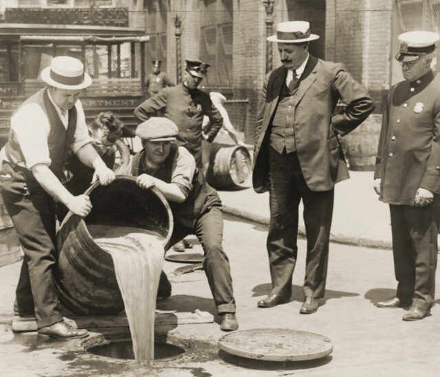 Men watch as other men dump a barrel of beer into the sewer.