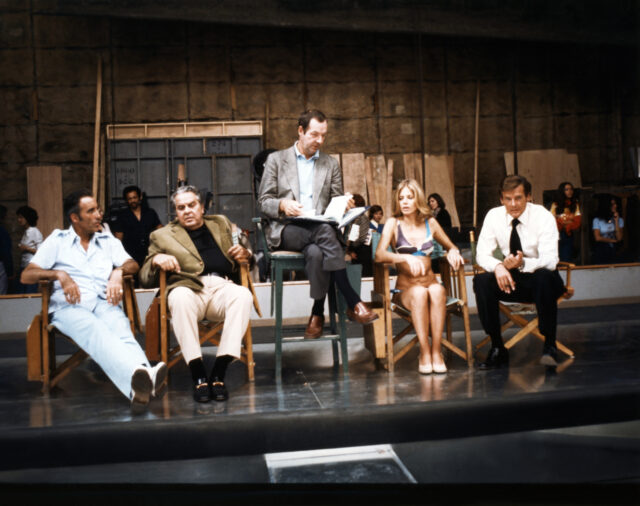 The cast and director of 'The Man With the Golden Gun' in chairs in a behind-the-scenes photograph.