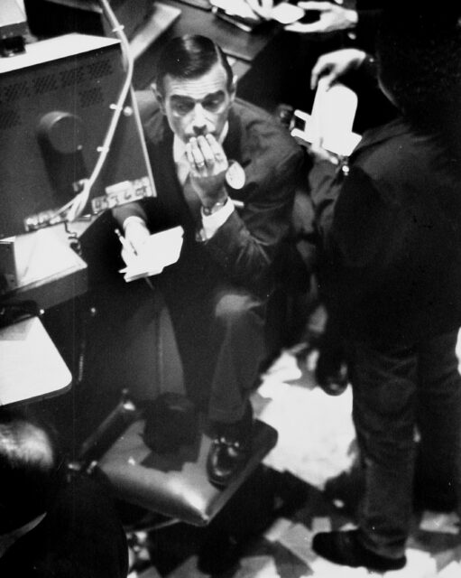 Stock broker resting on his knee on a chair, looking stressed out.