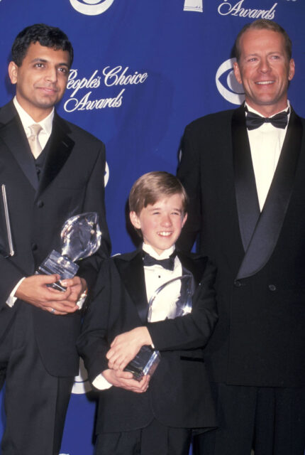 M. Night Shyamalan, Haley Joel Osment and Bruce Willis standing on a red carpet