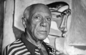 Headshot of Pablo Picasso in front of one of his paintings.