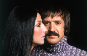 Sonny Bono looking forward, Cher's profile overlapping his face.