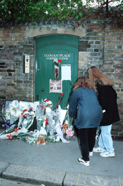 Two women leave flowers at the gate of a garden in honor of Freddie Mercury.