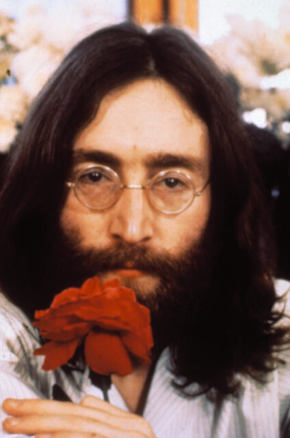 Headshot of John Lennon holding a red flower.