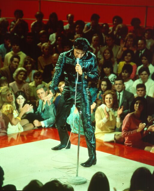 Elvis Presley performing of a stage, surrounded by people.