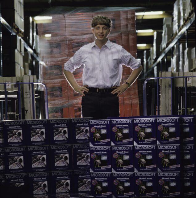 A young Bill Gates standing behind several Microsoft product boxes.