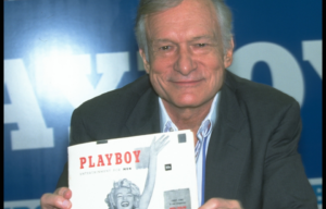 Hugh Hefner holding up a copy of the first-ever Playboy magazine.