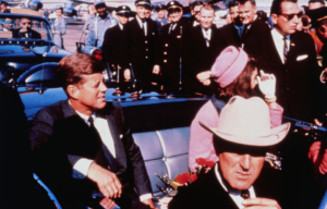 John F. Kennedy and Jacqueline Kennedy sitting in the back seat of an open-top car.