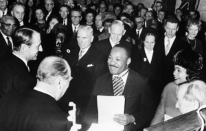 Martin Luther King Jr. smiling while surrounded by a crowd, holding a piece of paper.