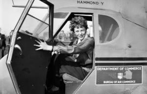 Amelia Earhart sitting in the cockpit of a plane with its door open.