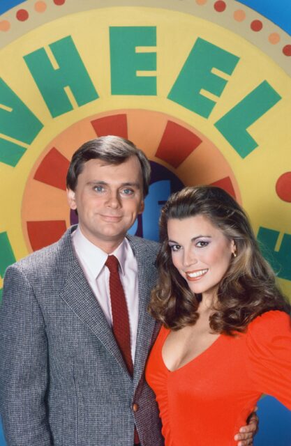 Portrait of Pat Sajak and Vanna White in front of a sign for the 'Wheel of Fortune.'