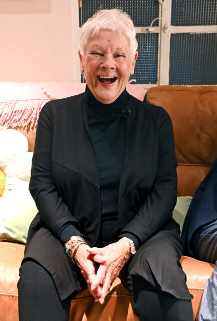 Judi Dench laughing while sitting on a couch