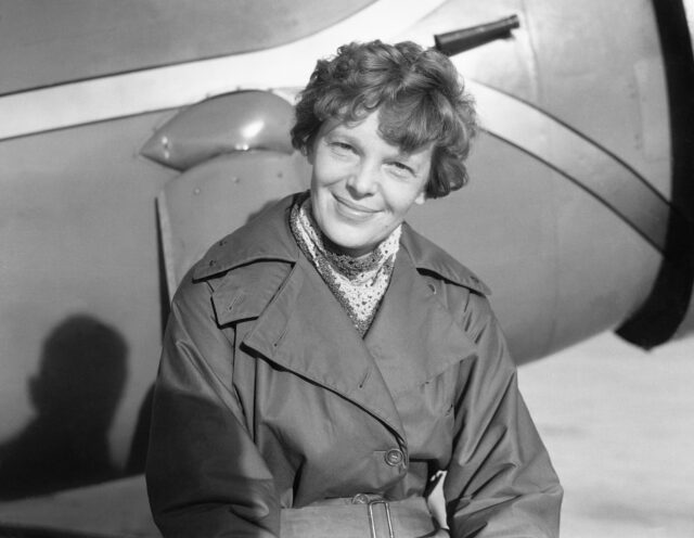 Amelia Earhart sitting and smiling in front of a plane.