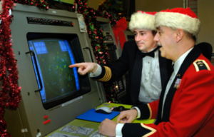 Two men pointing to a computer in Christmas attire.