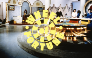 The opening shot of the game show 'Wheel of Fortune.' People standing at the wheel ready to play in the background.